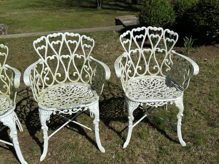 Two white ornate metal chairs on grass with heart-shaped backrests.