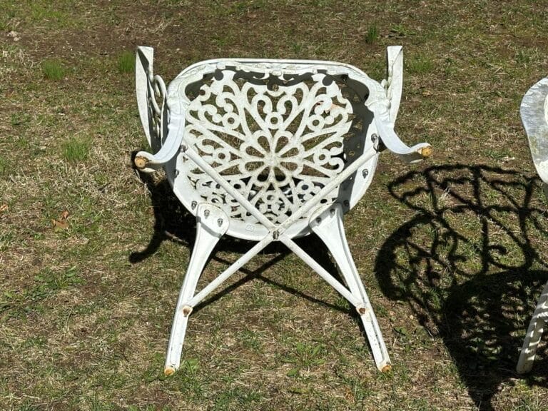 Upside down white metal patio chair with intricate floral design on grass.