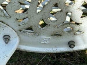 Close-up of a weathered white cast iron bench with bolts and a decorative pattern, set on grassy ground.