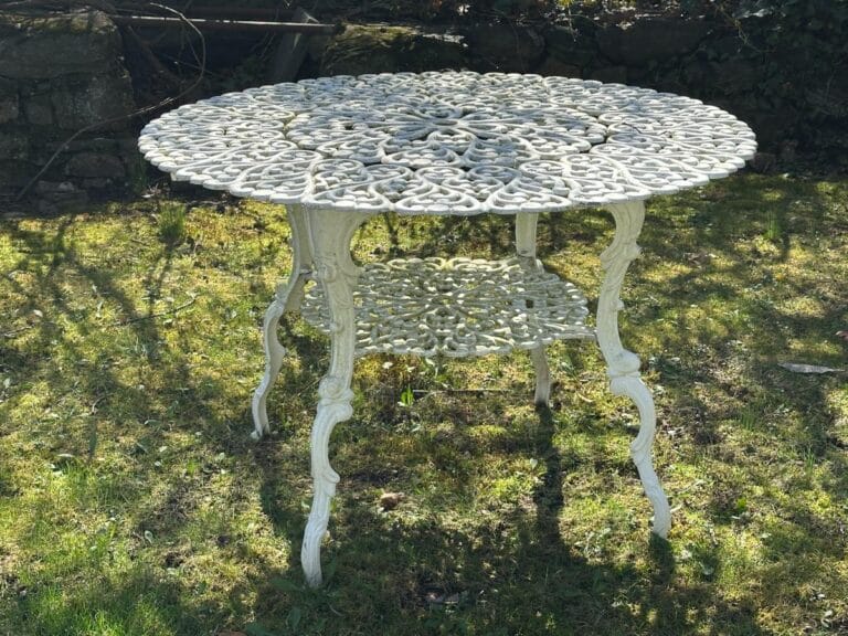 Ornate white metal garden table with intricate patterns, standing on grass.