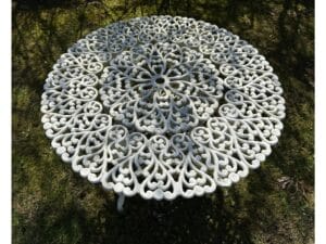 Ornate round metal table with intricate floral patterns, set on grassy ground.