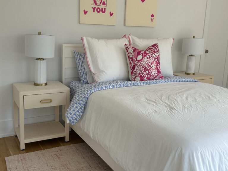 Cozy bedroom with white bed, pink and blue pillows, two lamps, and wall art above the headboard.